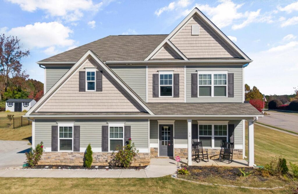 A two-story gray house with a brown shingle roof, dark shutters, and a front porch with stone accents.