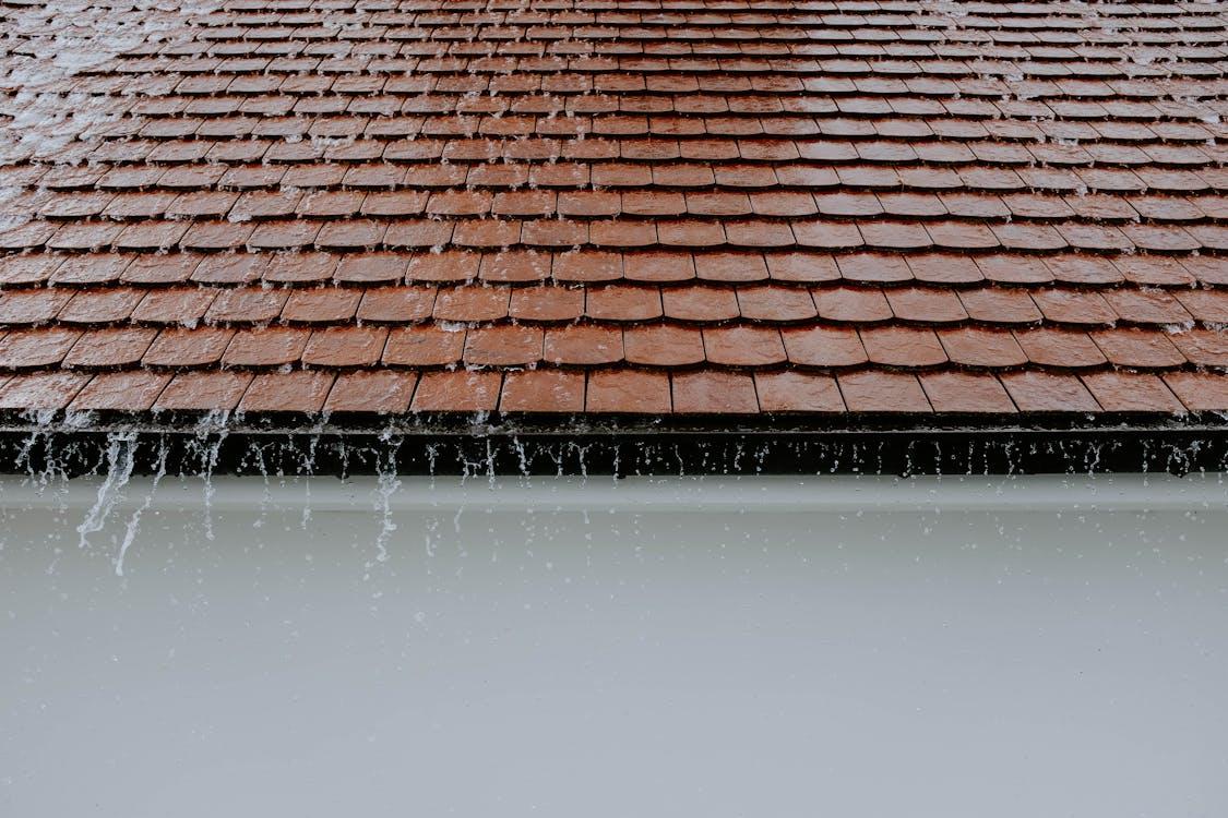 Rainwater flowing off residential roof shingles during a heavy rainfall